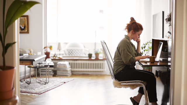 En ung kvinna sitter vid sin dator i ett stort vardagsrum. 