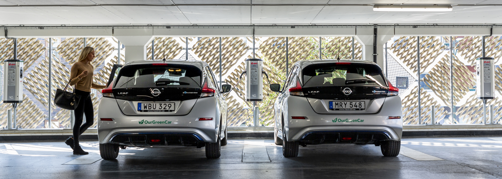 Två elbilar från bilpoolen står parkerade och laddar i ett garage. 