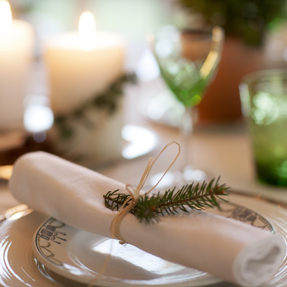 En julig dukning med vita servetter, snöre och grankvist.