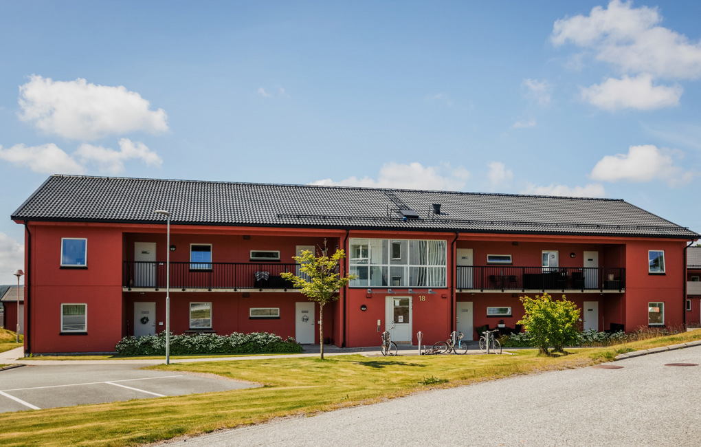 Ett rött hyreshus i två våningar med loftgångar och entredörrar på utsidan.