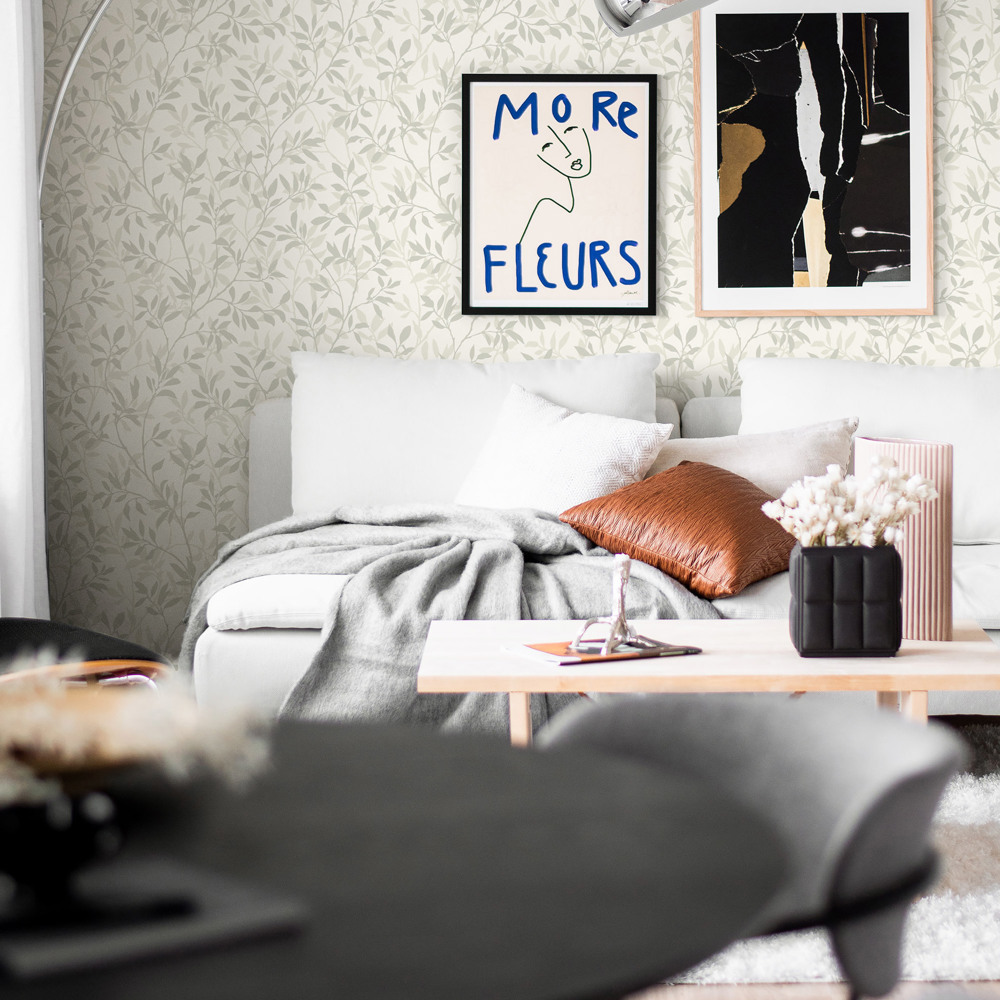 Ett vardagsrum med grönblommig tapet, soffa med en pläd slängd på. 