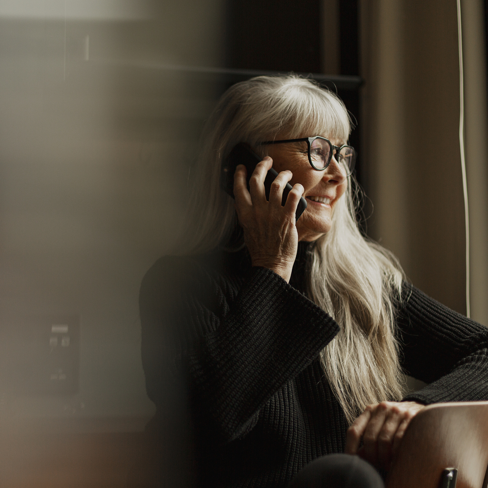 Kvinna pratar i telefon, ler och blickar ut genom fönstret.