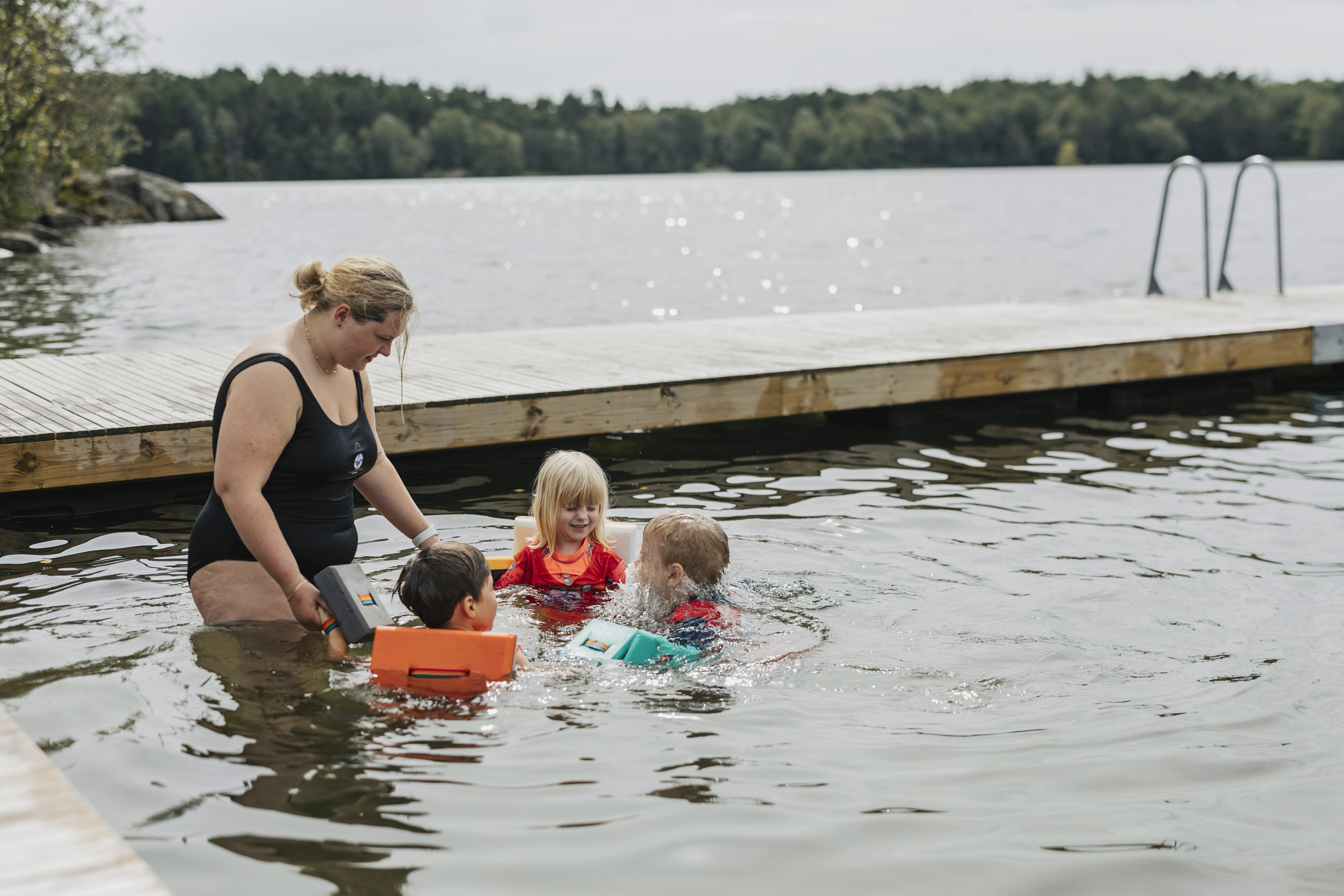 En simskolelärare tillsammans med några barn i ring samtalar i vattnet under simskolan.