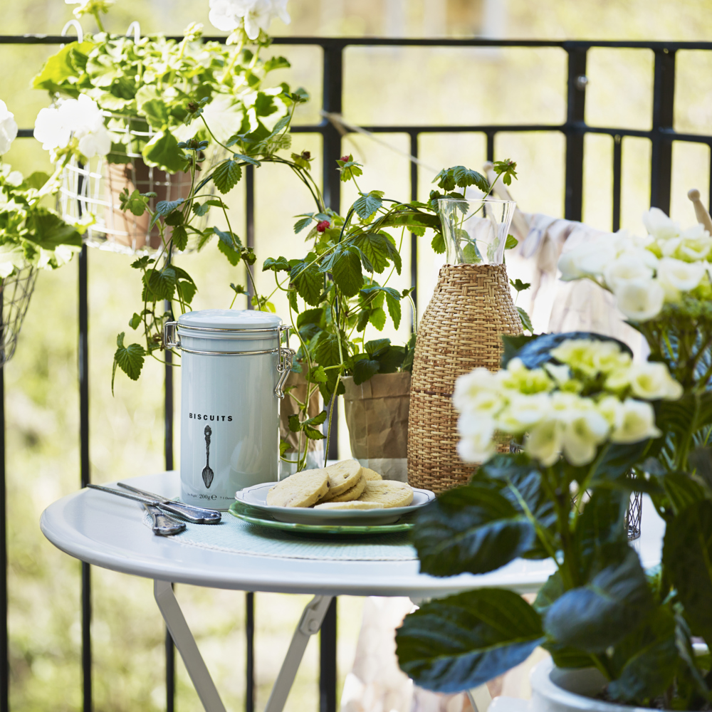 Dukat litet hopfällbart bord på en liten balkong tillsammans med växter och fika på bordet.