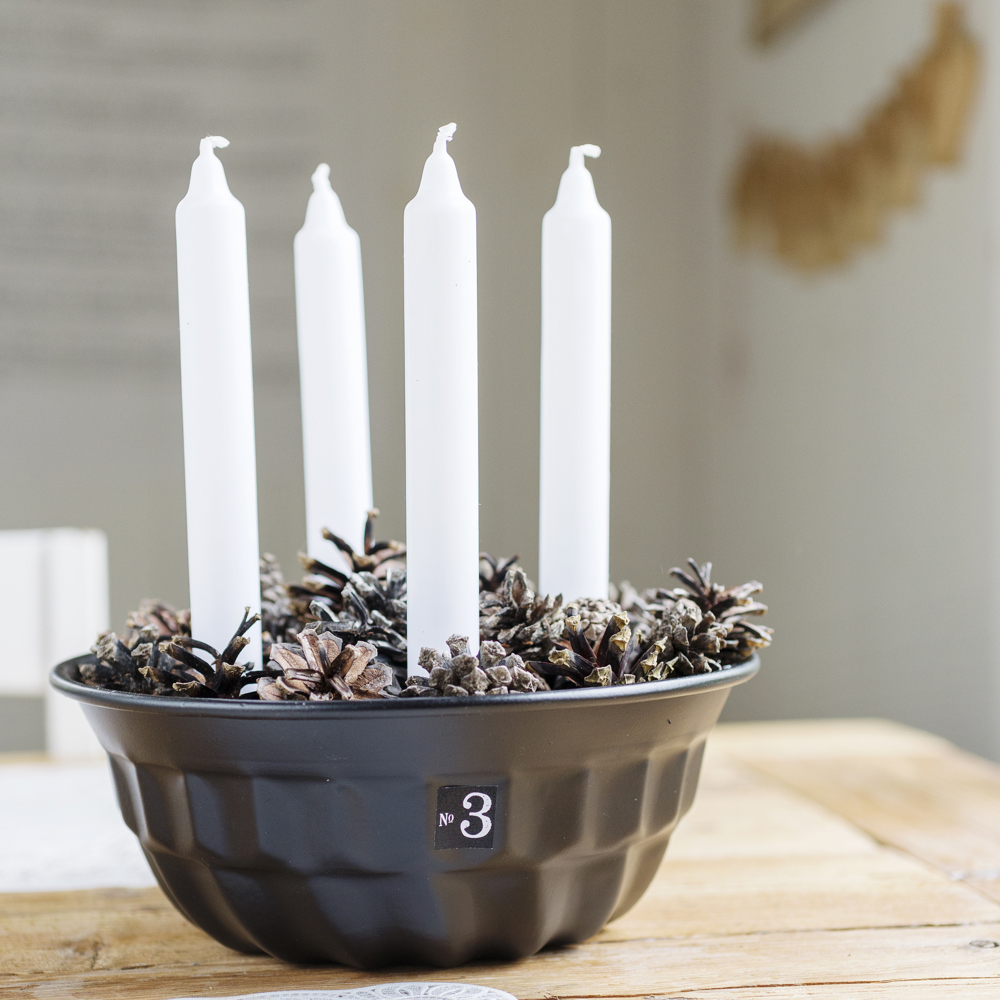 Fyra ljus i en bakform med kottar som dekoration.