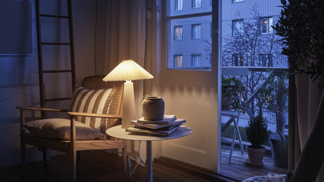 En bordslampa lyser upp i ett mörkt vardagsrum och skapar en mysig och hemtrevlig känsla.