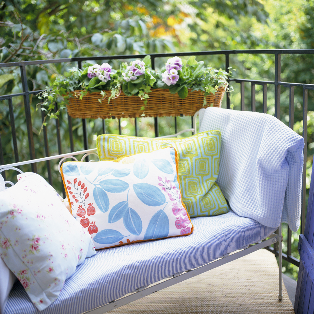 En soffa med kuddar och mjukpläd på en balkong med en blomsterlåda på insidan av räcket.