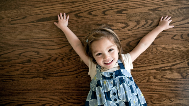 En leende liten flicka busar på ett mörkt parkettgolv. 