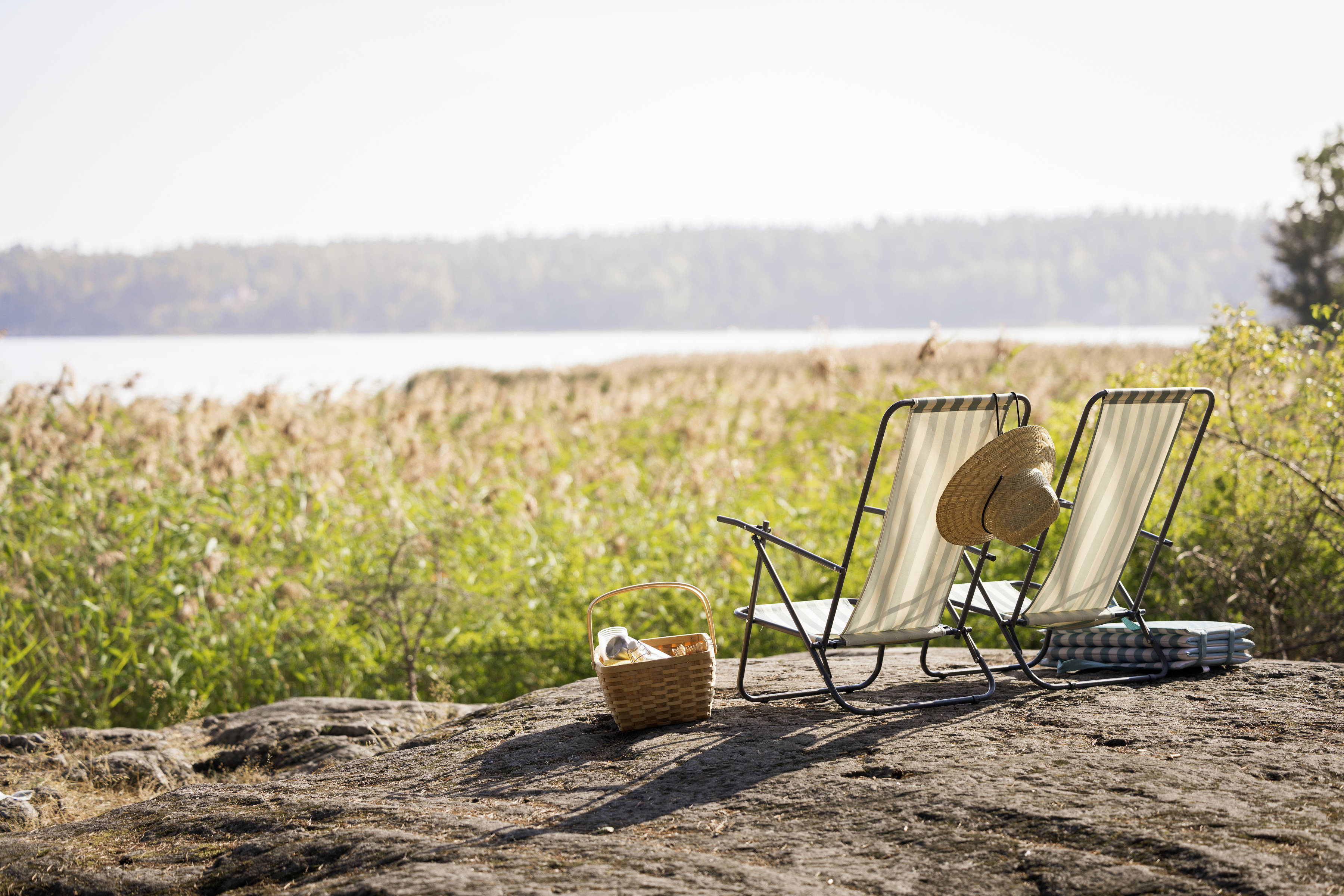 Sommarsolstolar står på en klippa och vetter ut mot en sjö.