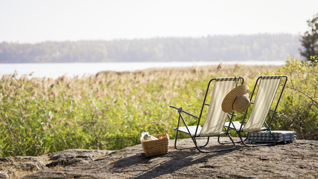 Sommarsolstolar står på en klippa och vetter ut mot en sjö.