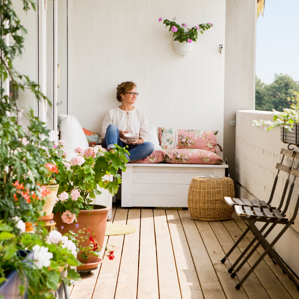 Kvinna njuter på sin balkong omgiven av växter en solig sommar dag. 