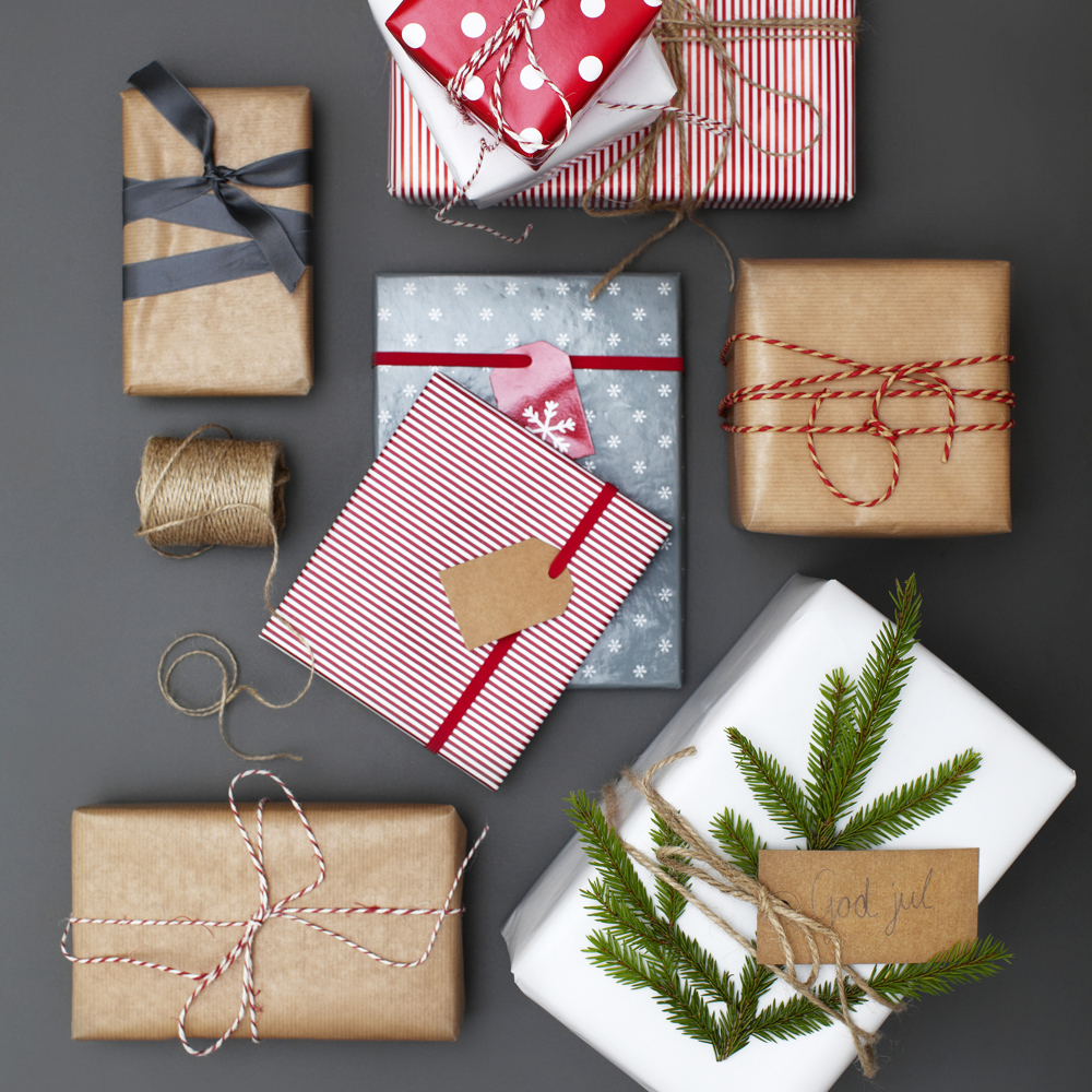 Julklappar i neutrala papper men dekorerade med fina band, snören och grankvistar.